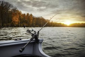 Fishing rod attached to a boat with the sunset over a calm lake.